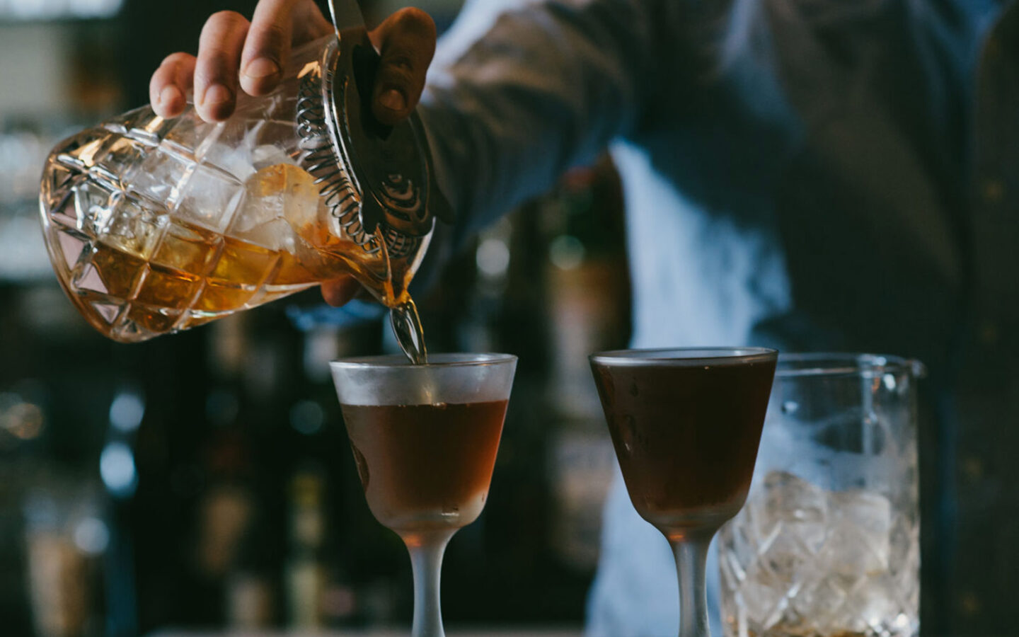 closeup of a bartender pouring a cocktail into a glass